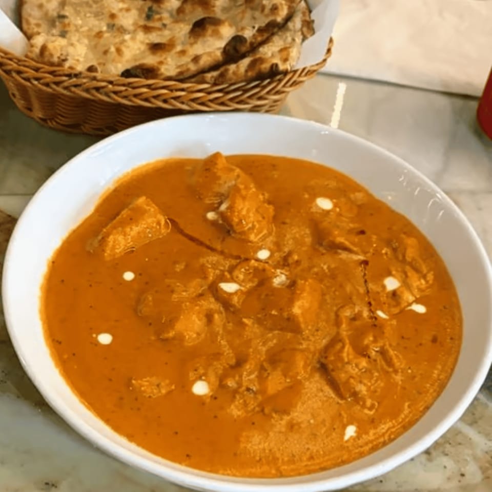 Chak De California's butter chicken in a white bowl with naan bread in a basket.