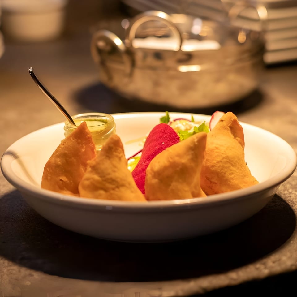 Golden-brown samosas with green chutney and a side salad in a white bowl at Chak De California.